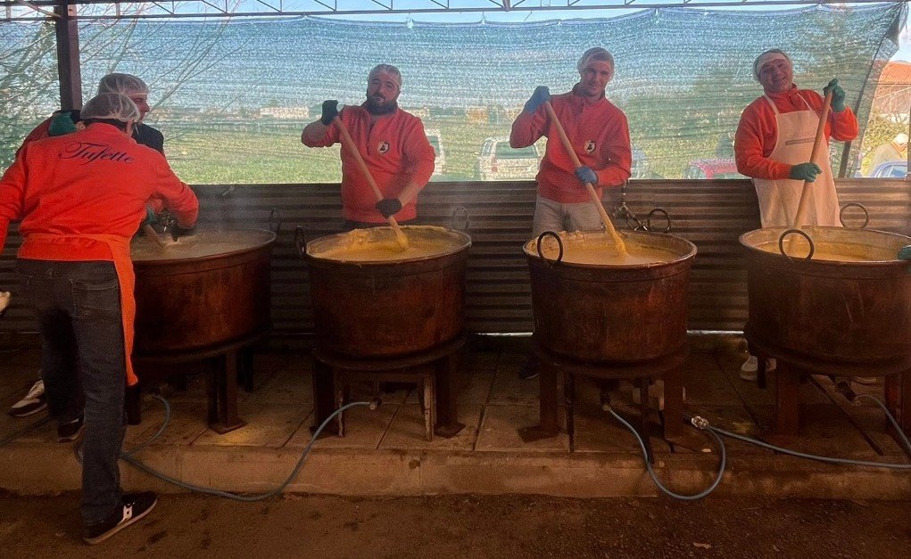Quattro volontari del Comitato mescolano la polenta nei paioli di rame allineati sotto la tettoia
